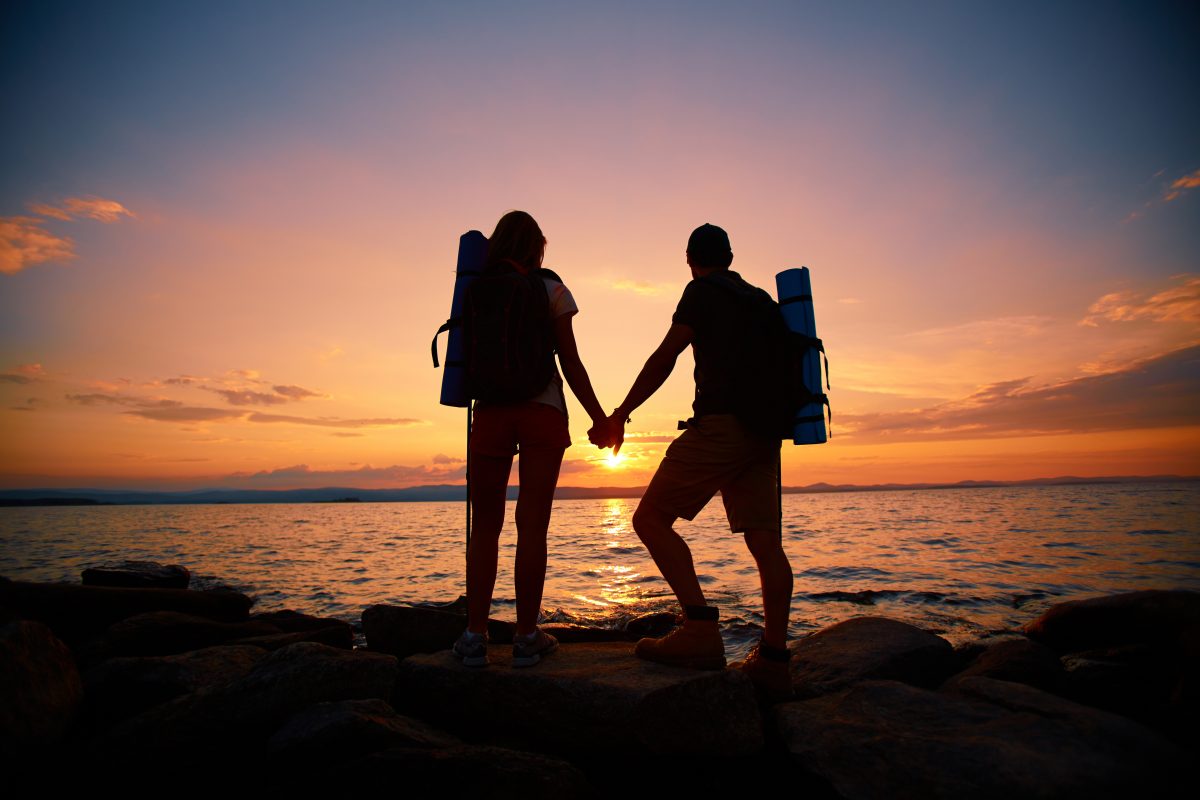 Image of beautiful scene of sunset and backs of couple of hikers enjoying it